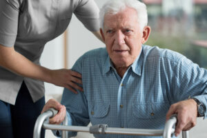 A carer helping an elderly man walk using a walking frame