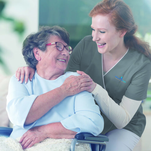 Carer placing her hands on an elderly patient's shoulder. Eldery patient is sitting on a wheelchair.